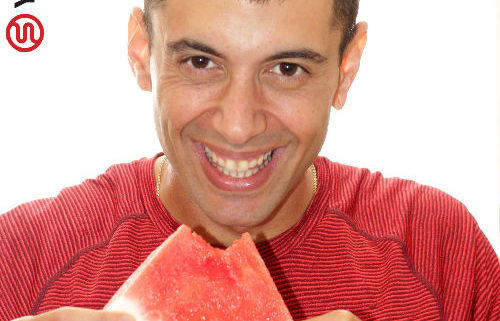 בחור בחולצה אדומה עם פלח אבטיח בידו מתוך פוסט כיצד לעבור את ארוחת ערב חג השבועות בשלום
