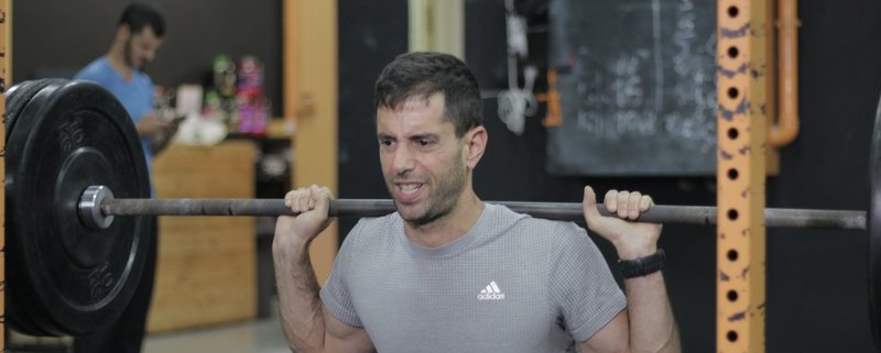 בחולצה אפורה מבצע סקווט כבד שלאחריו אין ספק מה זה מסה של משקל