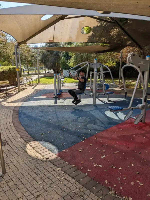 בבגדים כהים מתאמן בגינה על מכשיר בישיבה