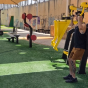 מה ההבדל בין פעילות אירובית לאנאירובית: למה כל אחת מתאימה ואיך לשלב ביניהן בחור בגופיה שחורה מבצע תרגיל לחיצת כתפיים עם מכשיר בתוך גינה עם מכשירי כושר